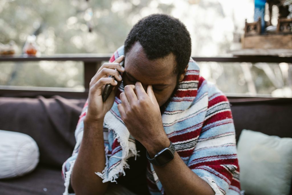 A man wrapped in a blanket looks distressed while talking on the phone outdoors.